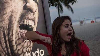 A tourist jokes in front of an advertisement with the portrait of Uruguay’s forward Luis Suarez at Copacabana beach in Rio de Janeiro, Brazil, on June 26, 2014. Sportswear giant Adidas said Thursday it would stop using Luis Suarez, one of its key promotional stars, for World Cup adverts after his four-month ban from football activities for biting Italian Giorgio Chiellini. AFP PHOTO / YASUYOSHI CHIBA