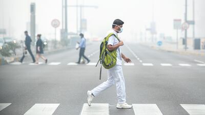 A healthcare worker crosses a street in central Abu Dhabi during foggy weather. Victor Besa / The National