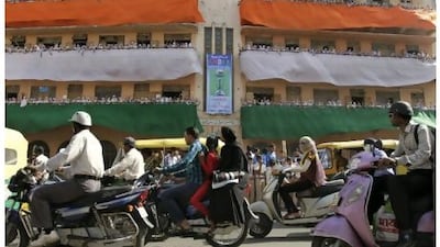 Indian commuters drive past as schoolchildren cheer for the India cricket team from a balcony in Ahmedabad yesterday. Ajit Solanki / AP Photo