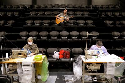 Volunteers wearing face masks to curb the spread of the new coronavirus sew face masks as a guitarist plays for them. AP