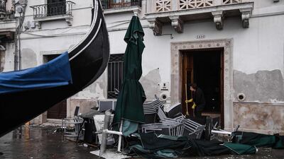 A woman clears a building entrance by piled-up cafe furniture and a stranded gondola. AFP
