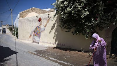 A woman sweeps the street next to a mural by Portuguese artist Mario Belem in the village of Erriadh, on the Tunisian island of Djerba. Joel Saget / AFP Photo