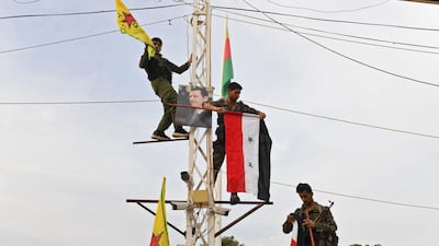 Syrian government soldiers climb up an electrical pole with the Syrian government national flag and the Kurdish People's Protection Units (YPG) yellow flag, along with a portrait of Syrian President Bashar Al Assad, by the Turkish border in the Syrian Kurdish town of Kobane. AFP