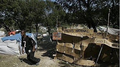 A man walks by a tent made of cardboard boxes with the sign "National Palace" in the Delmas 40 refugee camp for earthquake survivors in Port-au-Prince.