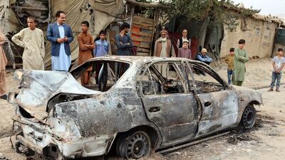 People stand by the shell of a vehicle damaged by a rocket attack. AP
