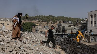 Ayat Abdullah, 31, with her daughter Aylar, one, on the rubble of the building, destroyed by the Israeli army, where she used to have a shop – her sole source of income