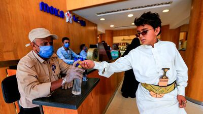 A security guard wearing a protective mask sprays sanitiser onto the hands of incoming customers as a measure against Covid-19 in Yemen's capital Sanaa. AFP