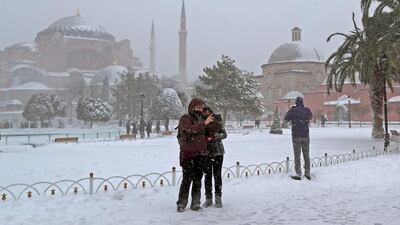 People enjoy taking a selfie in the snow in front of the Hagia Sophia Museum, left, in Istanbul. Tolga Bozoglu / EPA