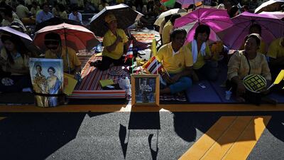 Well-wishers sit by portraits of Thai King Bhumibol Adulyadej and Queen Sirikit as they line up along the road leading to the Royal Palace where the King later marked the 64th anniversary of his coronation, in the seaside city of Hua Hin some 200 kilometres south of Bangkok. Christophe Archambault / AFP Photo