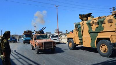 Smoke rises in the background from bombardment around the area as fighters with the Free Syrian army drive their pick-up truck, left, past a Turkey Armed Forces convoy in Idlib province. AP