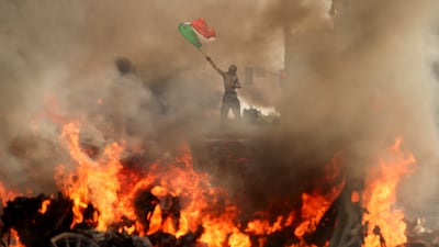A man waves a flag as smoke and flames rise from a burning vehicle during a protest against federal immigration in downtown Los Angeles. Reuters
