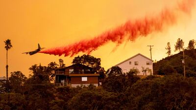 An airplane drops fire retardant over homes in the Spanish Flat area of Napa, California as flames rage through on August 18, 2020. AFP