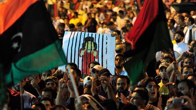 People wave flags of the Kingdom of Libya and hold a cartoon illustration of Libya's leader Muammar Gaddafi as they gather near the courthouse in Benghazi August 22, 2011 to celebrate the entry of rebel fighters into Tripoli. Jubilant rebel fighters strea???