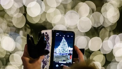 A woman takes a photo with a smartphone of a Christmas tree in front of the Brandenburg Gate in Berlin, Germany. Christmas markets have been cancelled in Berlin this year. EPA