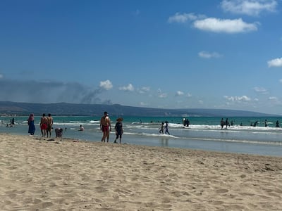 Plumes of smoke from nearby Israeli strikes rise over the hills in the background, as seen from the beach at Tyre. Nada Maucourant Atallah / The National