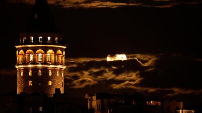 The moon is seen between clouds as it rises beside historical Galata Tower in Istanbul, Turkey. Reuters
