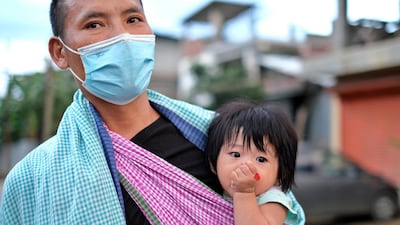 A man wearing a face mask walks with an infant on a sling in north-east Indian city of Imphal. AP Photo