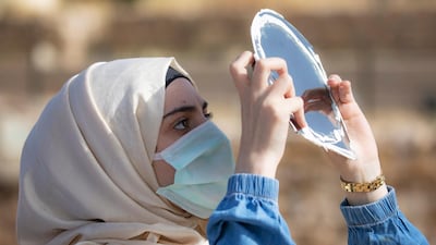 A woman wearing a face mask uses a mirror covered with a special filter to observe a partial solar eclipse at the Citadel in downtown Amman, Jordan. EPA