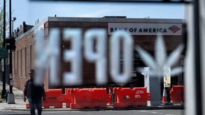 A man walks near a Bank of America as a marijuana leaf is seen on the open sign at the Sneaker Headz cannabis store April 15, 2022, in Washington. AFP