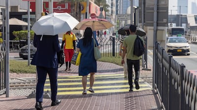 Pedestrians take cover from the summer heat in Dubai Marina. Antonie Robertson / The National