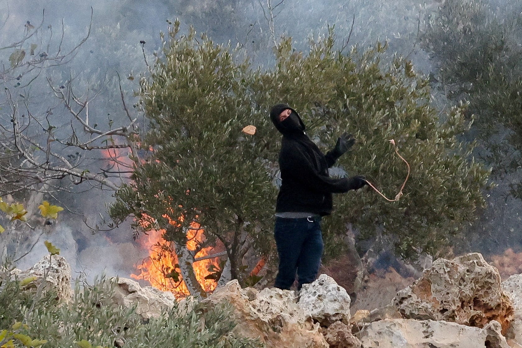 An Israeli settler casts a stone towards Palestinians, amid violence aimed at disrupting the Palestinian olive harvest, in Abu Falah, occupied West Bank. Reuters