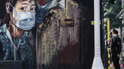 A police officer stands guard in front of a mural depicting a person wearing a face mask in Bogota, Colombia. AFP