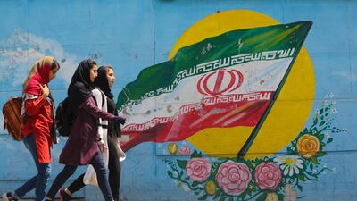 Young girls walk in front of a mural showing the Iranian national flag in the centre of the capital Tehran, on April 23, 2019. AFP