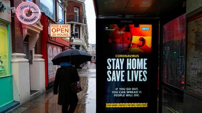 A pedestrians walks past NHS signage promoting "Stay Home, Save Lives" on a bus shelter in London. AFP