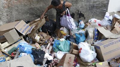 A woman searches through a street rubbish dump where pieces of large bone and meat are evident, adding to the community health hazards. Barbara Walton / EPA