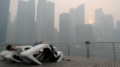 A man rests on a bench with Singapore’s central business district covered in haze in the background.