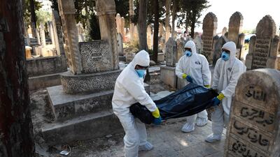 Health workers carry the body of a 62-year-old displaced Syrian man who died of Covid-19 to be buried in the town of Salqin, in the north-western Idlib province. AFP