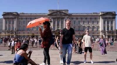 Tourists shelter from the sun as they stand outside Buckingham Palace in London. AP