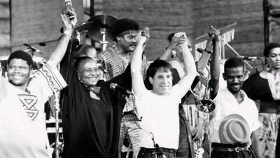 A still from the documentary Under African Skies, showing Paul Simon on stage with African performers during his Graceland tour.