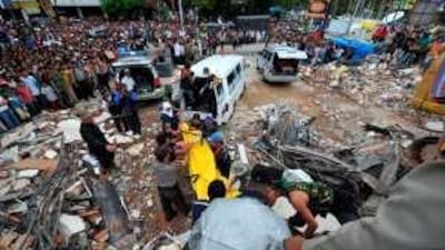 A young boy sits on a milk crate playing a guitar in the rubble of a destroyed village outside Apia in Samoa.