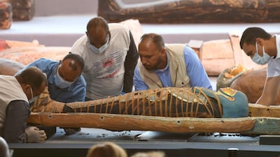 Archaeologists inspect a mummy, wrapped in a burial shroud adorned with brightly coloured hieroglyphics pictorials. AFP