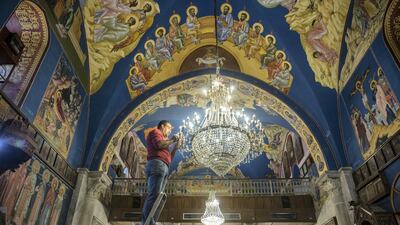 Rami Ayyad stands on a ladder as he carefully cleans the chandelier hanging from the the ceiling of the Church of Saint Porphyrius.