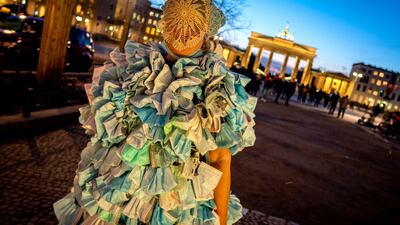 A woman wears a dress made of hundreds of face masks as she returns from an anti- coronavirus demonstration in Berlin. In the background is the Brandenburg Gate. AP