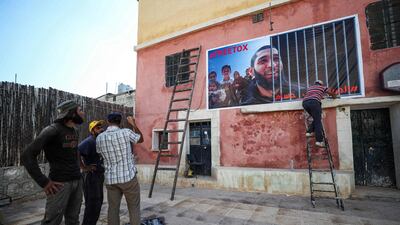 Men fix up a banner on the side of a building calling for the release of Tauqir Sharif, a self-described aid worker stripped of his British nationality and detained by Hayat Tahrir Al Sham (HTS) in Syria's rebel-held northwestern Idlib province. AFP