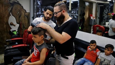 In this Friday, July 14, 2017 photo, Muhannad Khaled Omar, right, prepares to create an image of U.S. President Donald Trump on the back of a customer's head at his barber shop in Burj al-Barajneh, southern Beirut, Lebanon. In a city full of hair stylists, Omar stands out. He is a 26 year-old Palestinian-Syrian hair stylist known for shaving celebrity portraits into clients’ hair. (AP Photo/Bilal Hussein)