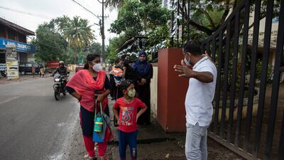A school staff member gestures to parents waiting outside the gate to maintain social distancing.