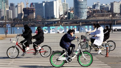 Young people wearing face masks ride bicycles at a park in Seoul. AP Photo