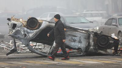 A man walks past a car that was overturned and destroyed during the protests in Almaty. Reuters