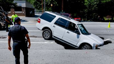 A police officer surveys the scene after an SUV was partially swallowed by a sinkhole on Ponce de Leon Avenue in Atlanta, in the south-eastern US state of Georgia. EPA