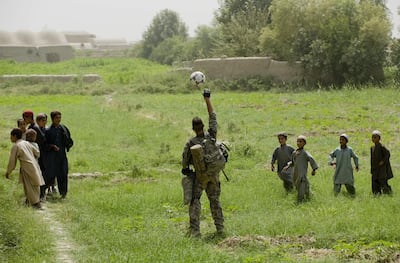 A US soldier plays football with Afghan children in Dand district of Kandahar province, Afghanistan. AFP