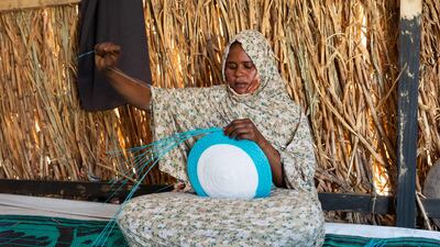 Twenty-three-year-old Sudanese refugee and student Asha Mohamat Mousa weaves a dish with plastic threads inside her shelter in the Tongori refugee camp