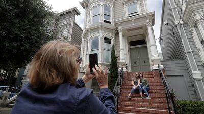 Aries Layton, seated left, and her aunt Kelsy Layton pose as Debra Layton, Aries' grandmother and Kelsy's mother, foreground, takes photos outside a Victorian home made famous by the television show "Full House" in San Francisco, Tuesday, July 17, 2018. Tour buses will no longer be swinging by the San Francisco house made famous in the popular 1990s sitcom "Full House." The San Francisco Municipal Transportation Agency voted Tuesday to ban commercial vehicles from Broderick Street after neighbors complained. (AP Photo/Jeff Chiu)