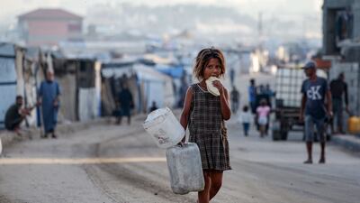A displaced Palestinian girl eats bread as she walks barefoot carrying empty gallons along a street in Deir El Balah in the central Gaza Strip. AFP
