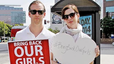 Adam Schulman and his wife Anne Hathaway hold up signs showing their support for the Bring Back Our Girls campaign. Courtesy Anne Hathaway