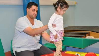 Hamda al Awadhi, 3, balances with help from physiotherapist Almontaser-Billah al Ghoun.