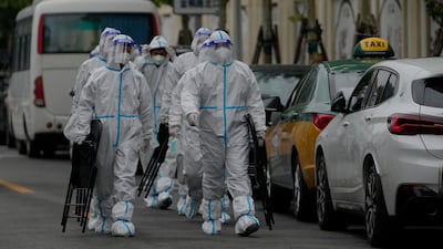 Health workers in protective suits carry foldable chairs as they head to a locked-down residential complex in Beijing on May 8. AP